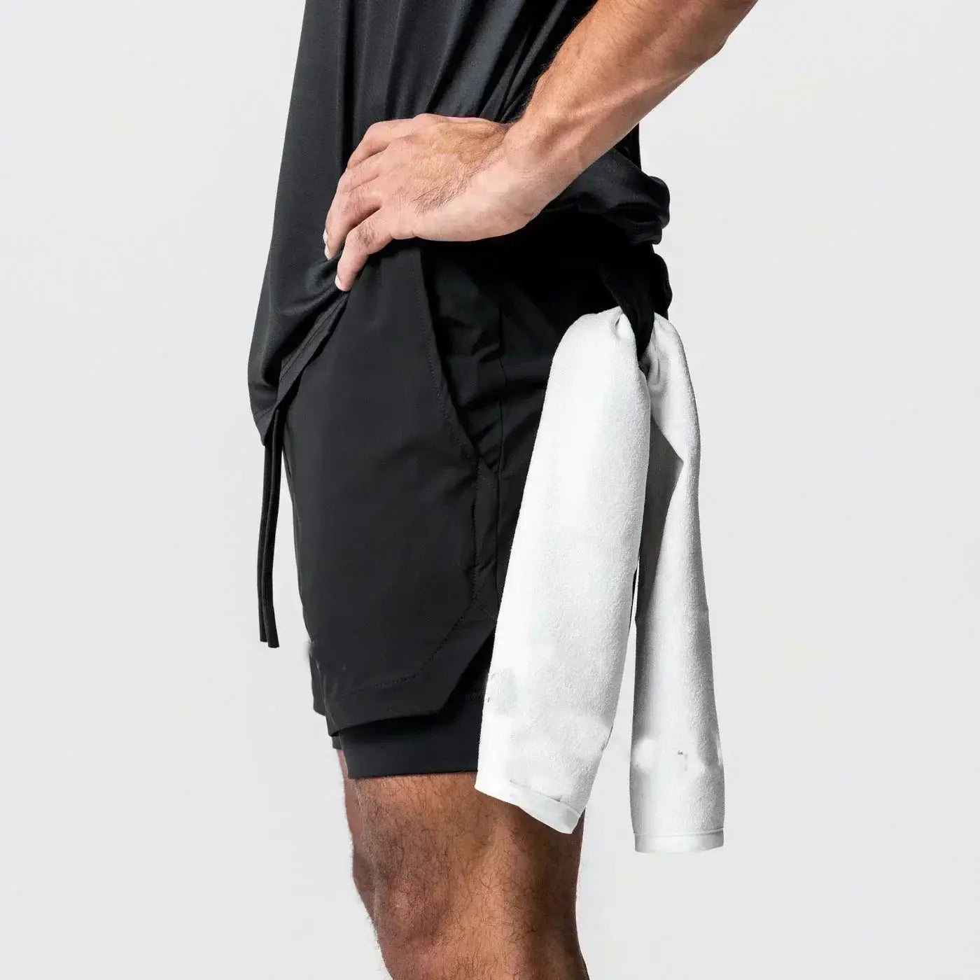 Pantalones cortos atléticos negros 2 en 1 para gimnasio con trabilla para la toalla y una toalla blanca atada alrededor de la cintura elástica, diseñados para uso en entrenamientos.