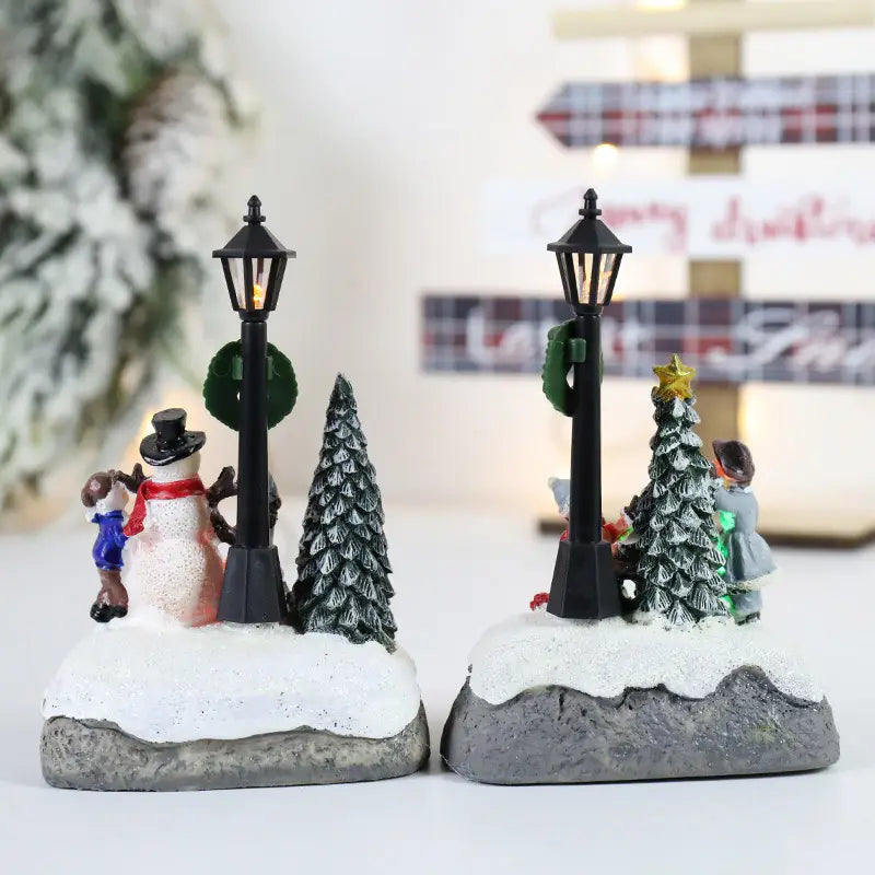 黒いランタンポストに、発光する電球を備え、雪の積もった台座が特徴の、クリスマスハウスライトLED雪だるまディスプレイ用のミニチュア・フィギュリン2体。各体が黒いランタンポストを備えています。
