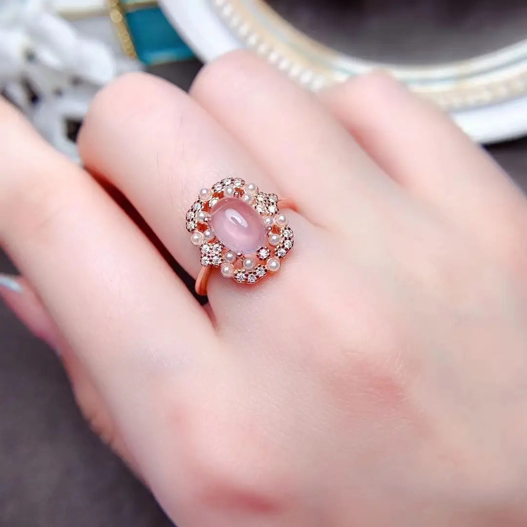 Une bague délicate en or rose, présentant une pierre de jade rose ovale au centre, entourée de diamants étincelants et de petites perles, provenant d’un ensemble de bijoux en argent sterling avec quartz rose.