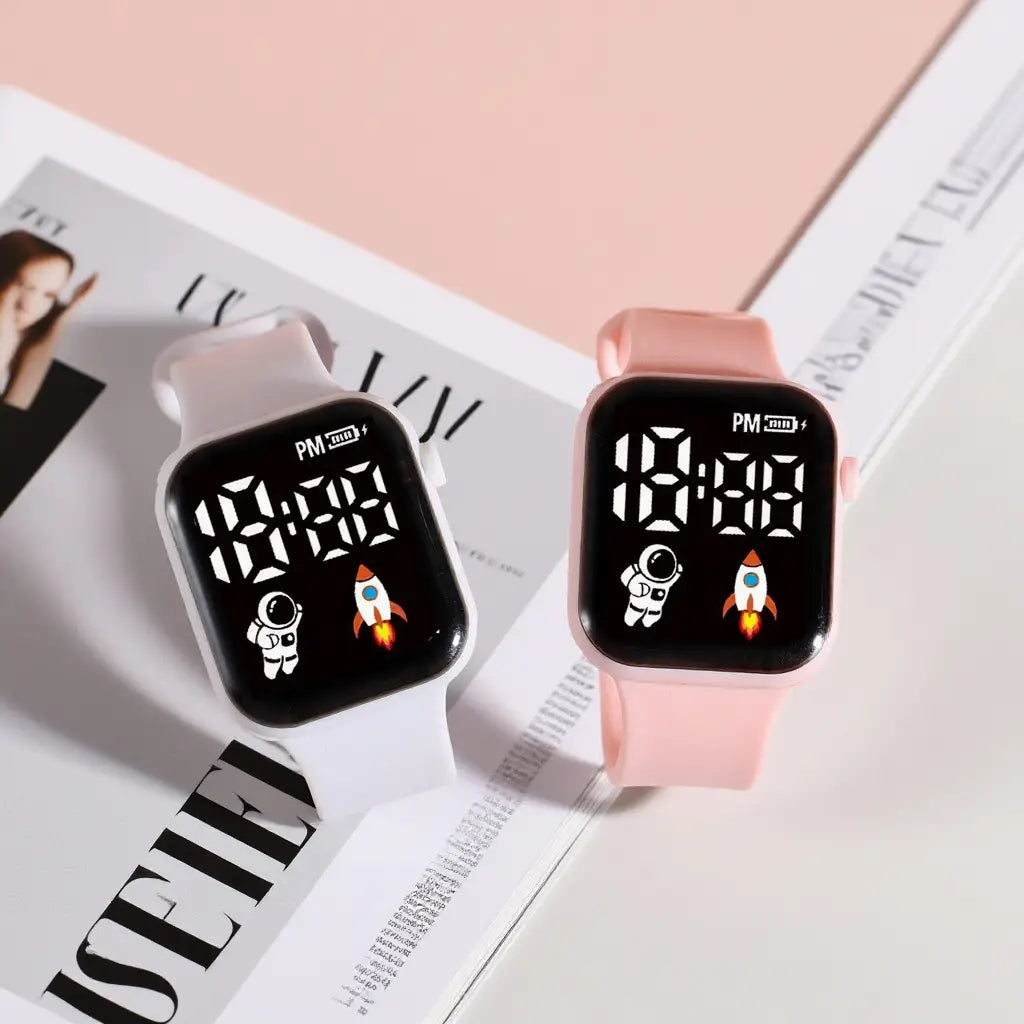Deux montres électroniques pour enfants, garçons et filles, avec motifs d’astronaute et de fusée sur écrans noirs, bracelets en silicone blanc et rose, dans un style de montre numérique LED de type sport.