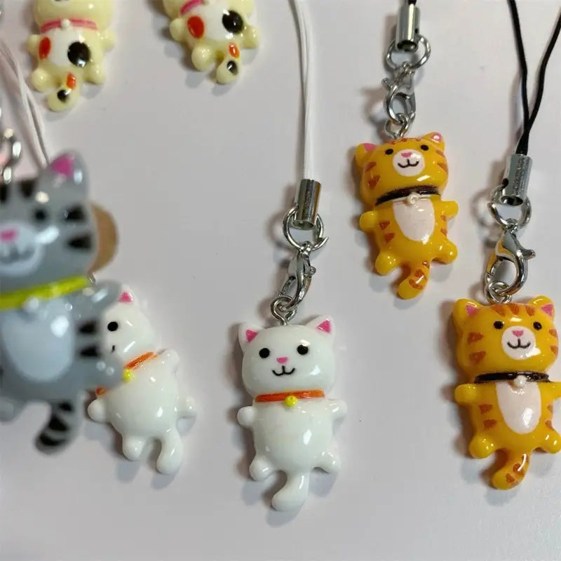 Cute cat phone charm strap featuring a yellow and white cat design with pink ears, an orange collar, and a metallic silver clasp.