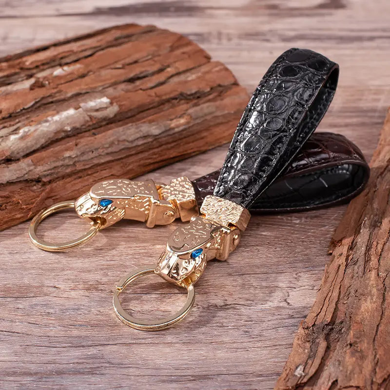Black crocodile-patterned leather keychain with gold-toned jaguar head charms featuring blue gemstone eyes for luxury car key ring use.