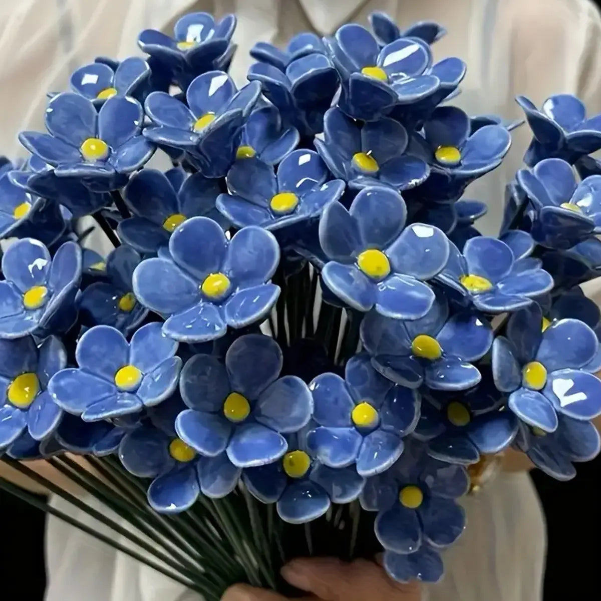 A bouquet of artificial flowers featuring glossy blue ceramic forget me nots with bright yellow centers ideal for decorating vases.