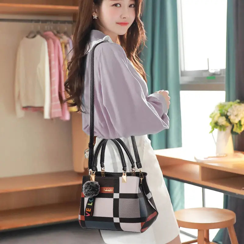 Black crossbody handbag pu leather satchel style1 style2 featuring black and white checkered pattern with a colorful love strap gold-tone hardware and fuzzy pom-pom charm.