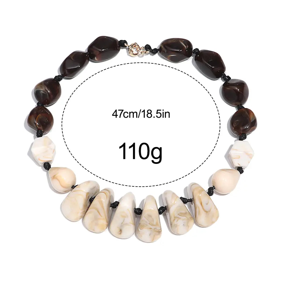 Collier ras du cou en résine à motif géométrique, fait de perles marbrées, avec alternance de perles en pierre marbrée brun foncé et crème, enfilées sur un cordon noir, muni d’une petite attache métallique.