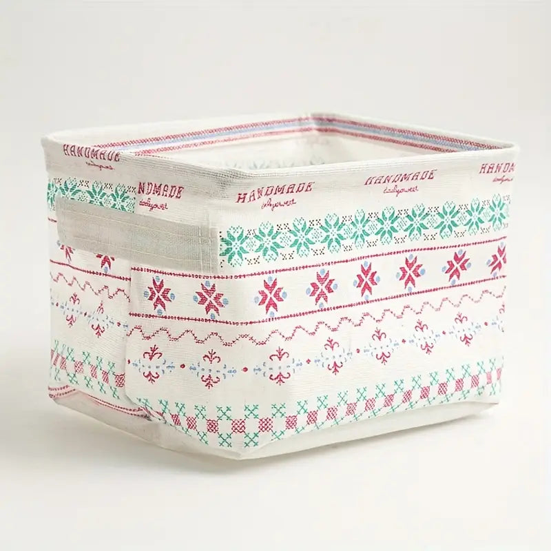 Panier de rangement pliable en tissu blanc avec des motifs nordiques brodés rouge et turquoise, et un texte fait main le long du bord supérieur, adapté comme boîte de rangement décorative.