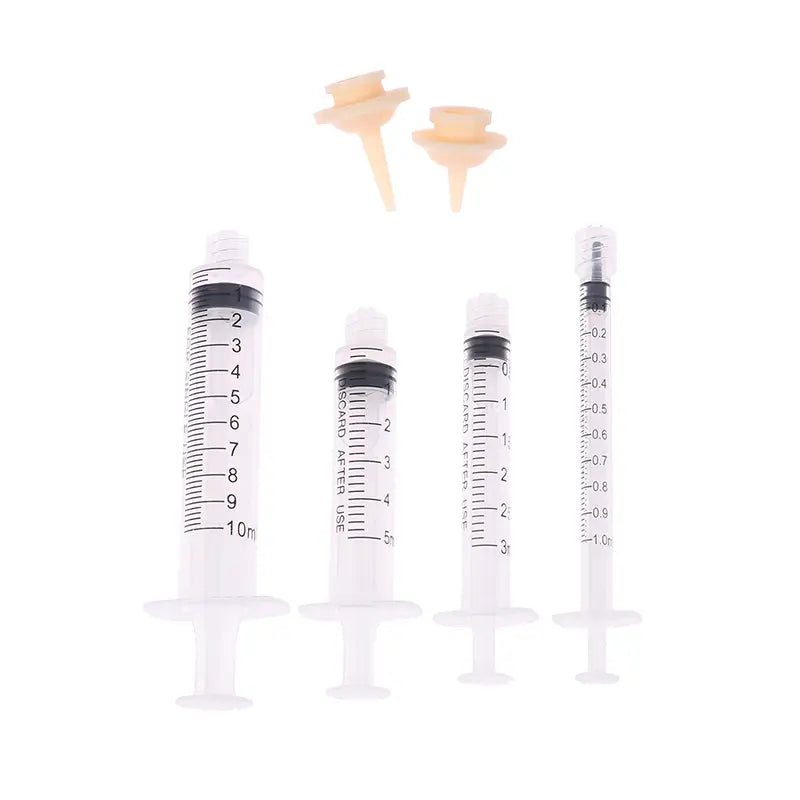 Set of four clear plastic pet oral syringes with black measurement markings and white plunger caps accompanied by two beige silicone nipples for feeding.