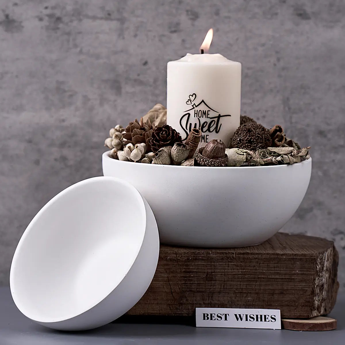 White ceramic round silicone mold with matching lid filled with dried botanicals and a lit white candle reading home sweet home for concrete storage bowls and candles.