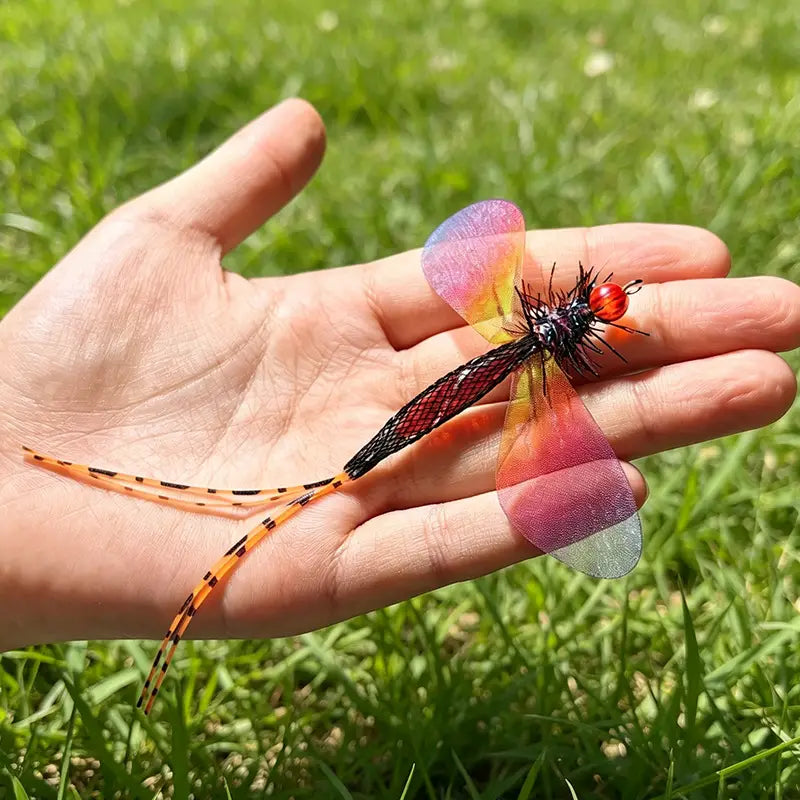 Ein lebhaftes durchscheinend eingefärbtes Libellen-Cat-Toy-Ersatzkopfteil mit schillernden rosa- und orangefarbenen Flügeln, einem schwarzen Netz-Körper, der mit roten Perlen verziert ist, sowie gestreiften Antennen.