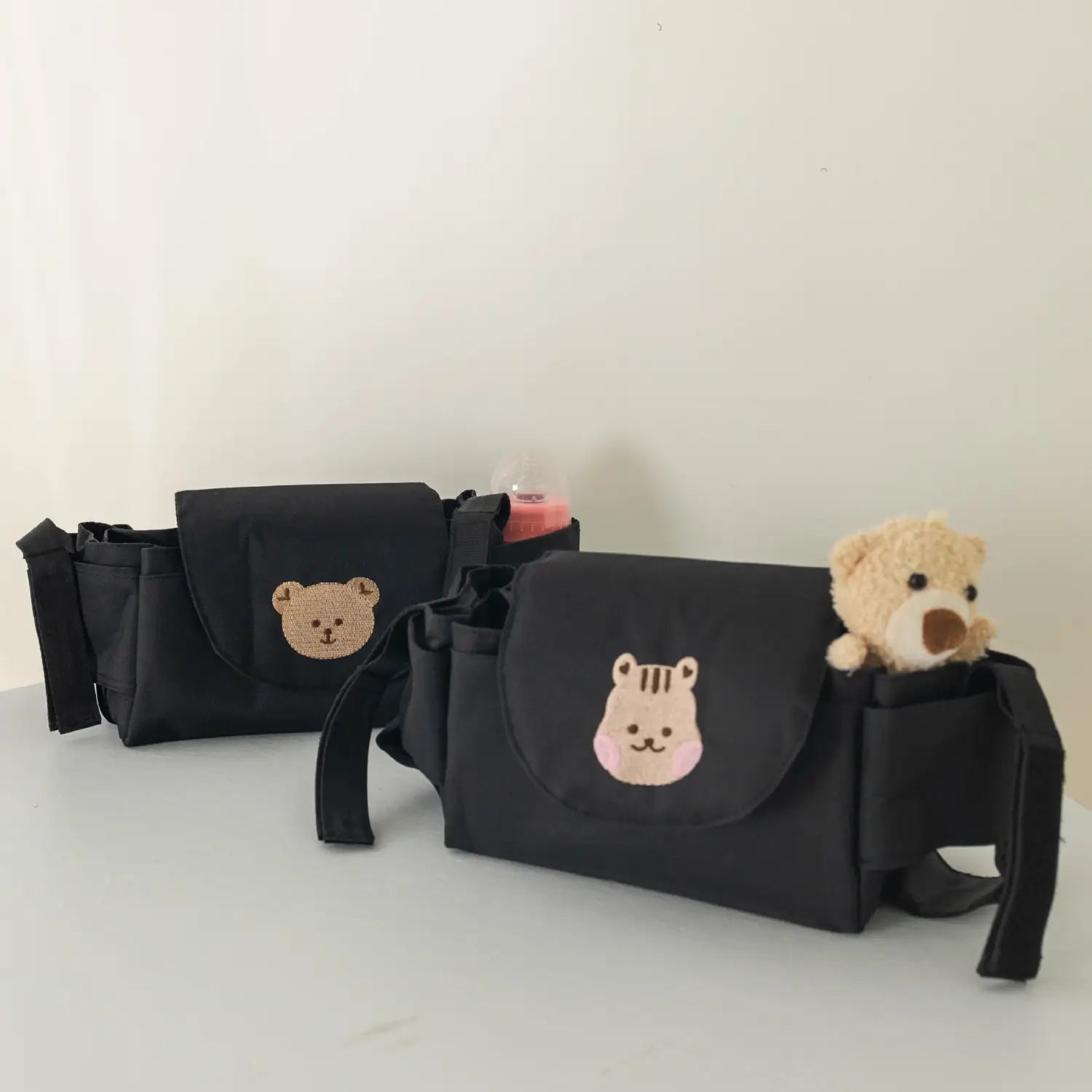 刺繍のクマの顔と、ぬいぐるみの玩具がのぞくデザインのブラックの布製ベビーカー用オーガナイザーバッグ。外出時の収納に便利。