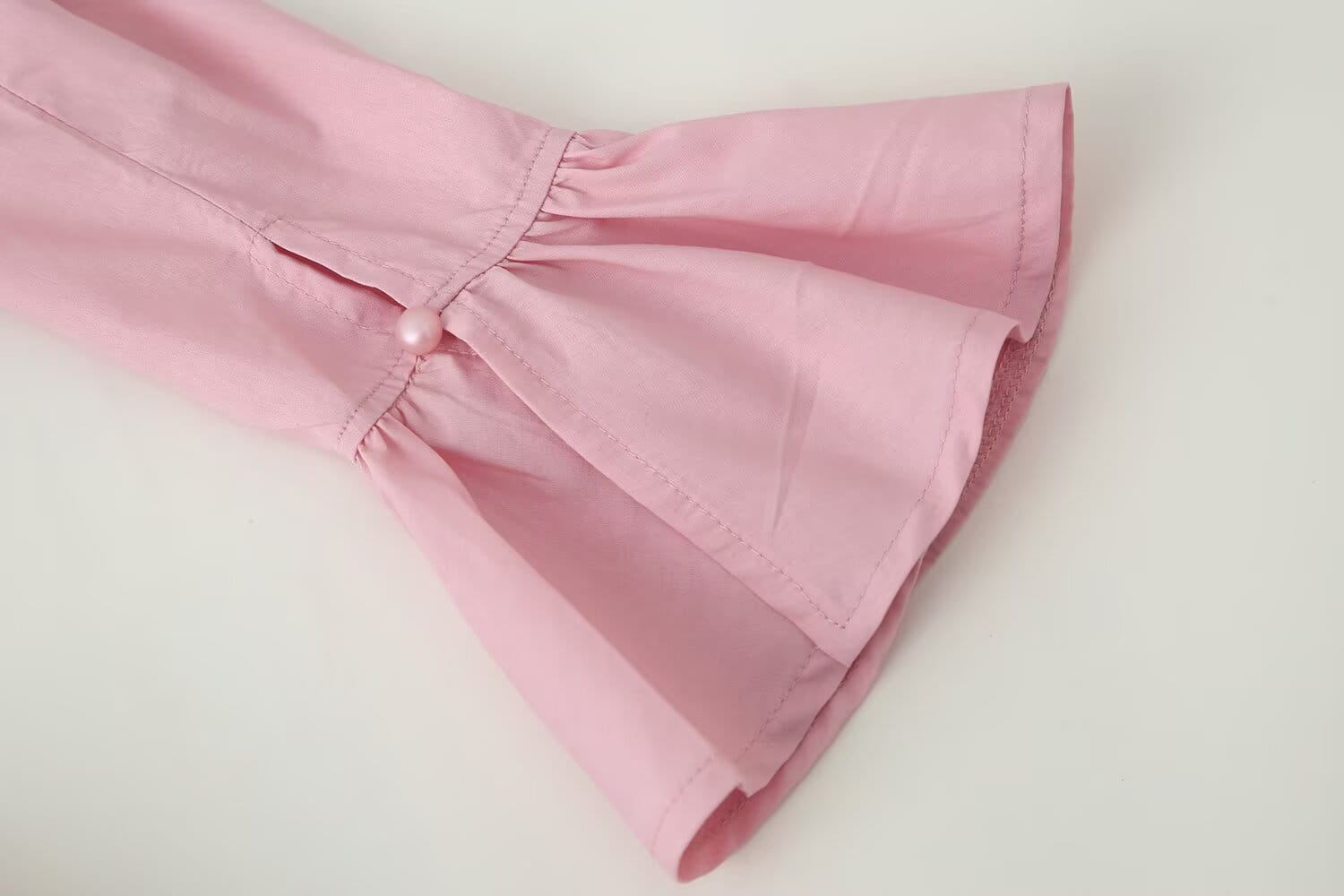 a soft pink women slim fit long sleeve round neck top featuring flared sleeves with delicate pearl buttons at the cuffs