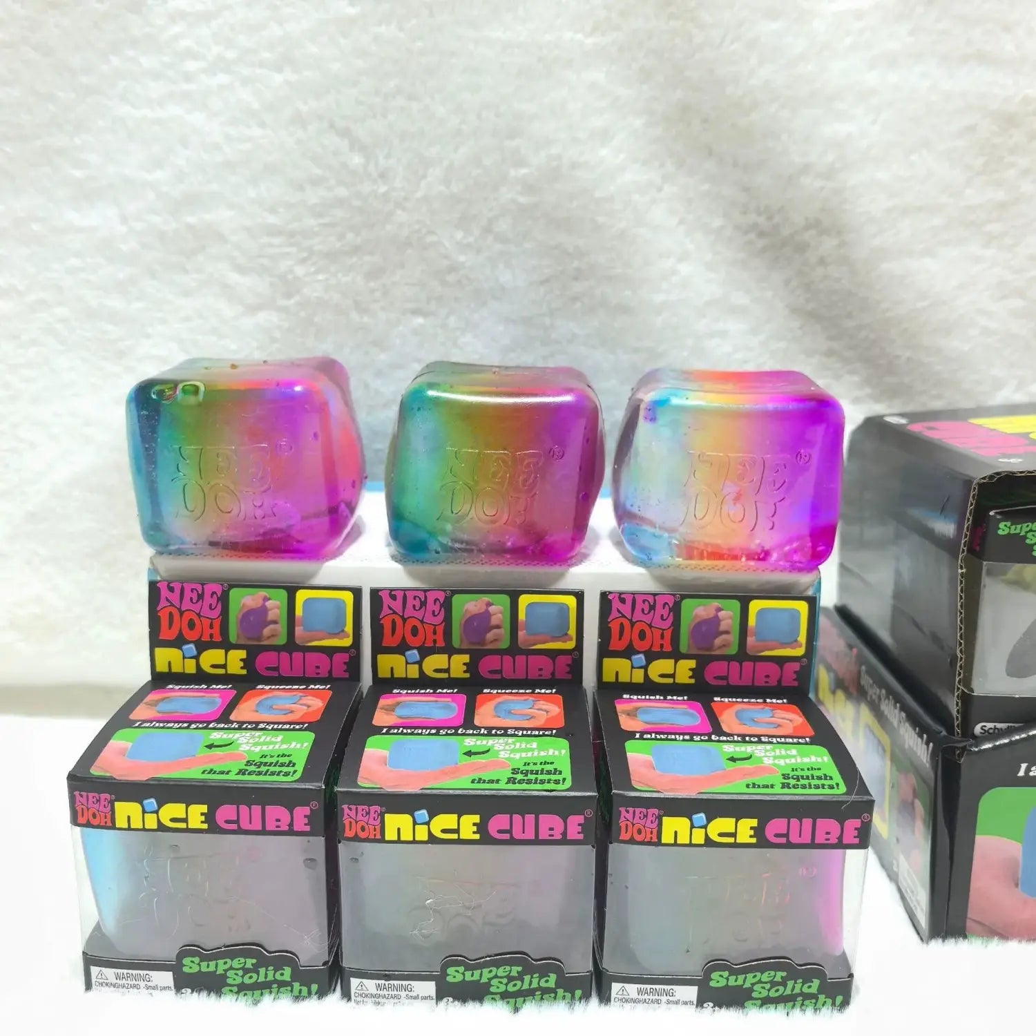 Eine Vorderansicht eines regenbogenfarbenen, transparenten Needoh-Würfel-Knet- und Fidget-Spielzeugs in seiner Originalverpackung.