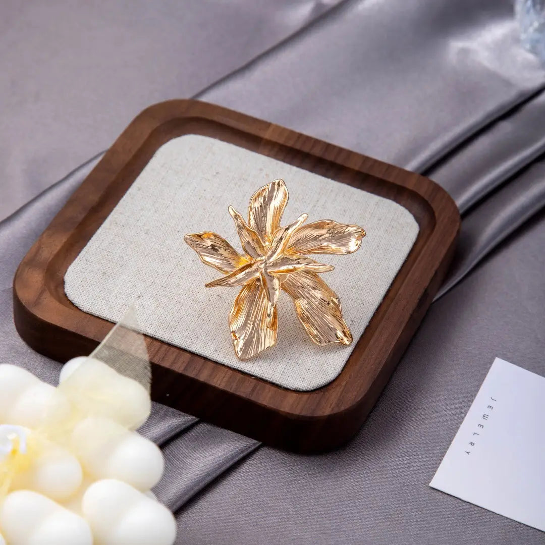 A delicate gold-toned adjustable double layer flower ring with intricate petal details displayed on a wooden tray.