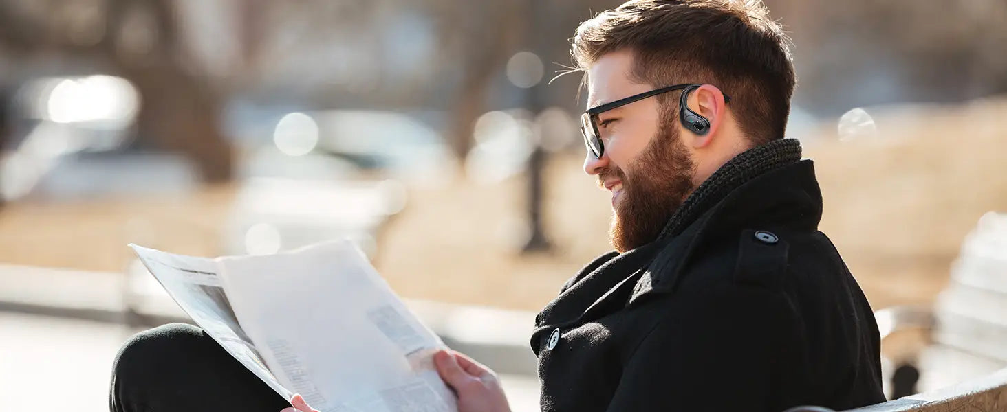 Un homme portant des écouteurs sans fil noirs au design minimaliste élégant, avec des crochets d’oreille et un boîtier de charge pour une recharge pratique.