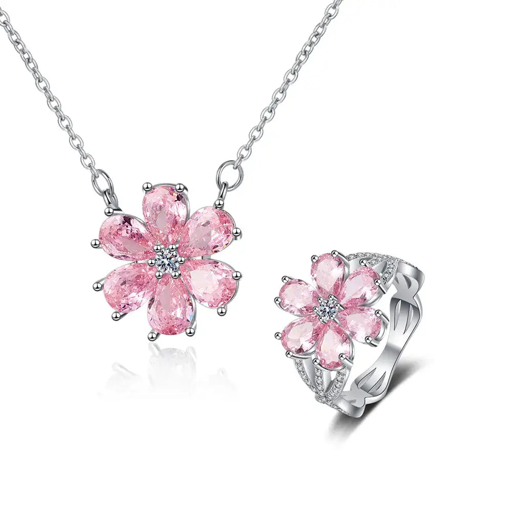 Ein zartes Set aus einer silberfarbenen Kirschblüten-Halskette und einem passenden Ring mit leuchtend pinkfarbenen, tränenförmigen Steinen, die in einem floralen Design angeordnet sind, mit funkelnden klaren Akzentsteinen im Zentrum.