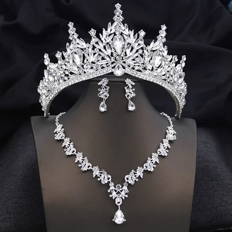 Une couronne de mariée étincelante en argent et un ensemble de bijoux, comprenant des feuilles en cristal aux détails complexes et des pierres en forme de goutte, avec des boucles d’oreilles et un collier assortis présentant un motif floral, pour des accessoires de mariage.