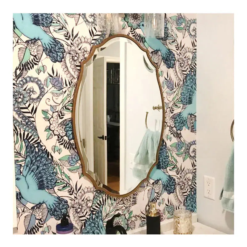 Miroir de salle de bains ovale avec un cadre ornemental doré monté sur un mur, mettant en valeur un papier peint raffiné à motif d’oiseaux et de fleurs bleu et noir, pour un style de miroir élégant.
