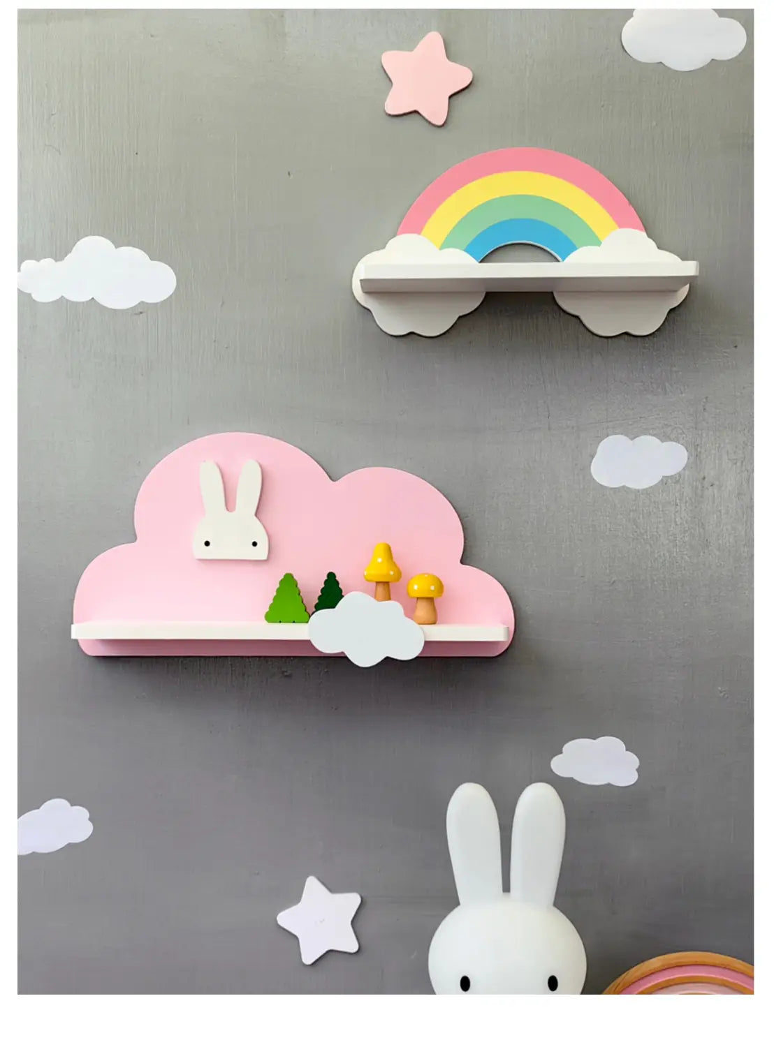 Ein rosa, wolkenförmiges Bücherregal aus Holz für Kinder an der Wand mit einem weißen Hasen und Miniaturbäumen oben drauf im Design einer Regenbogenwolke.