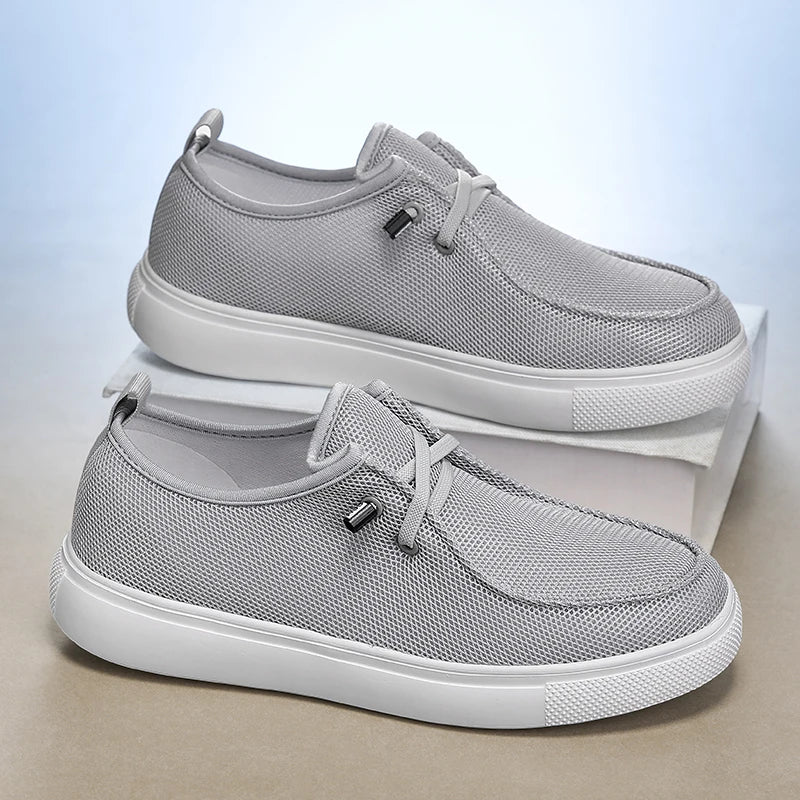 Chaussures de type mocassins décontractées pour hommes en maille gris clair, dotées d’un matériau en maille respirant, de semelles en caoutchouc blanc et d’œillets métalliques noirs.