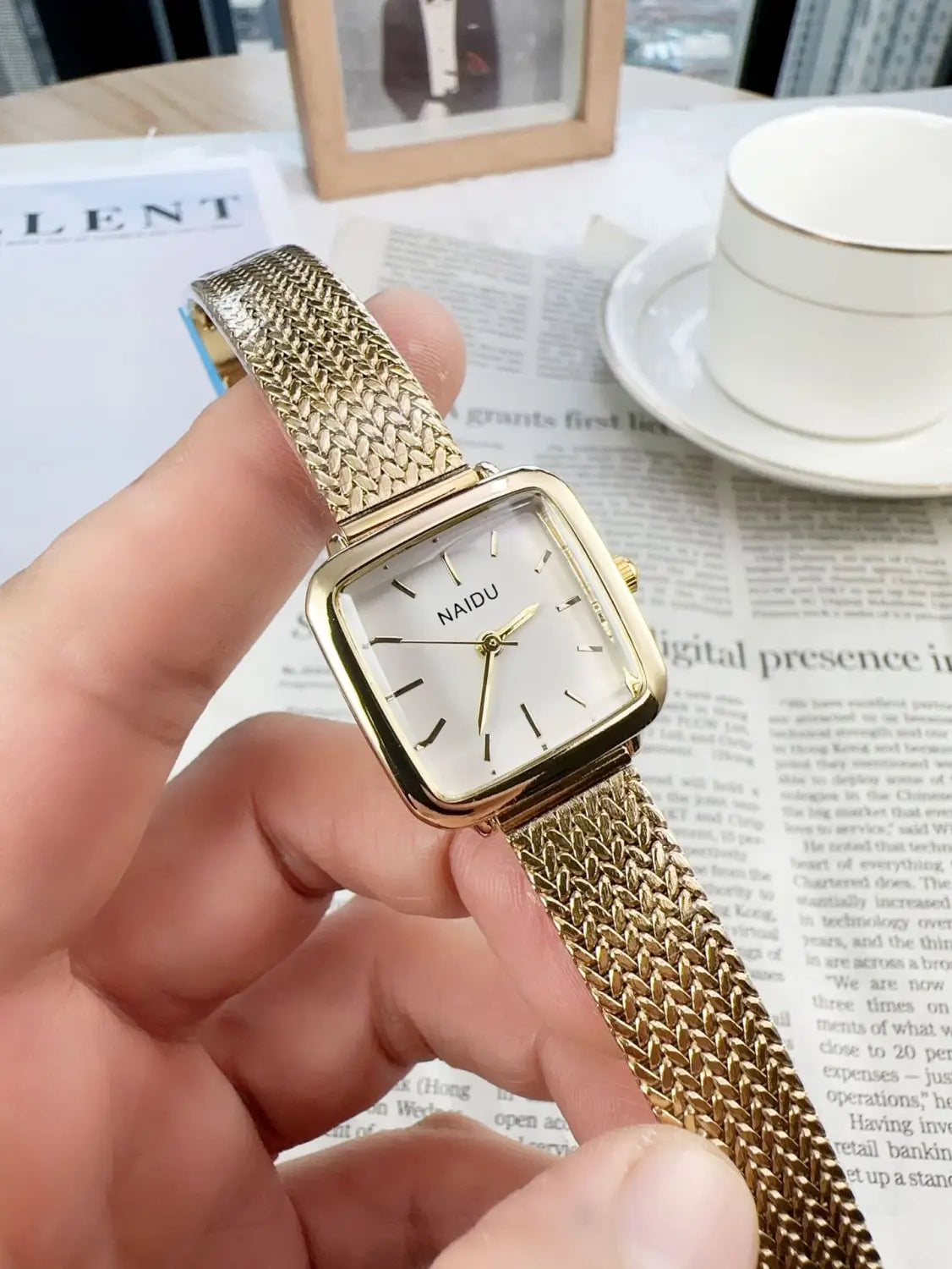 Minimalist square quartz watch for women with a gold mesh strap and a square face featuring a minimalist silver dial with the brand name naidu.