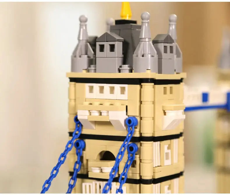 Un modèle d’architecture en briques de construction de type Tower Bridge, en briques Lego, beige et gris, avec des chaînes bleues suspendues sur les côtés.