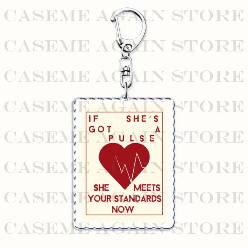 A rectangular Gracie Abrams acrylic keychain with a cream-colored background and red text reading if she’s got a pulse she meets your standards now above a bold red heart with an ekg line design and a silver metal clasp.