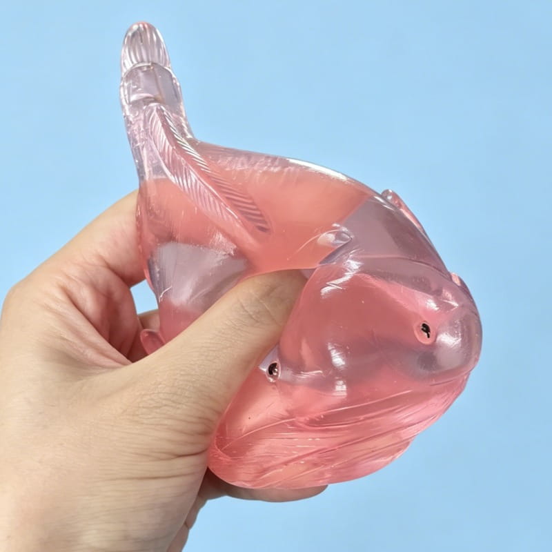 Un relaxant anti-stress translucide en forme de poisson, rose, avec des écailles détaillées et une finition légèrement brillante, provenant du coffret de jouets anti-stress à mâcher « baleine » en matériau souple.