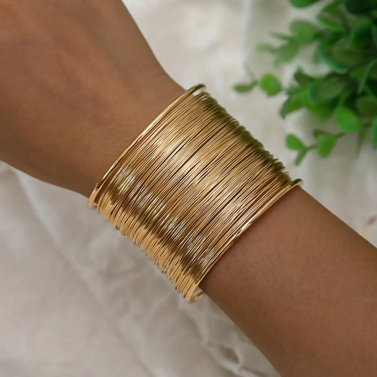 Un ensemble de bracelets manchettes en fil fin plaqué or, superposés, portés au poignet, mettant en valeur un design de bijouterie élégant