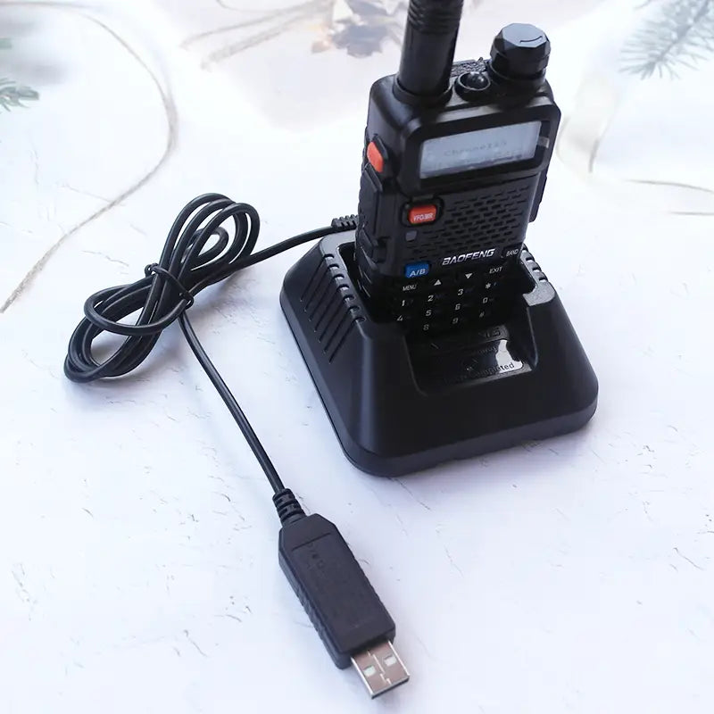 Talkie-walkie Baofeng BF-888S noir avec câble de charge USB torsadé posé à côté de son chargeur de bureau noir assorti, pour une connexion de câble de charge USB efficace.