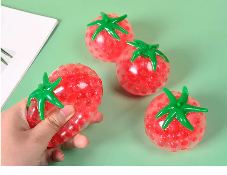 Red tomato-shaped squishy stress relief toy with green plastic stem and translucent gel beads inside for squeezing and stress relief.
