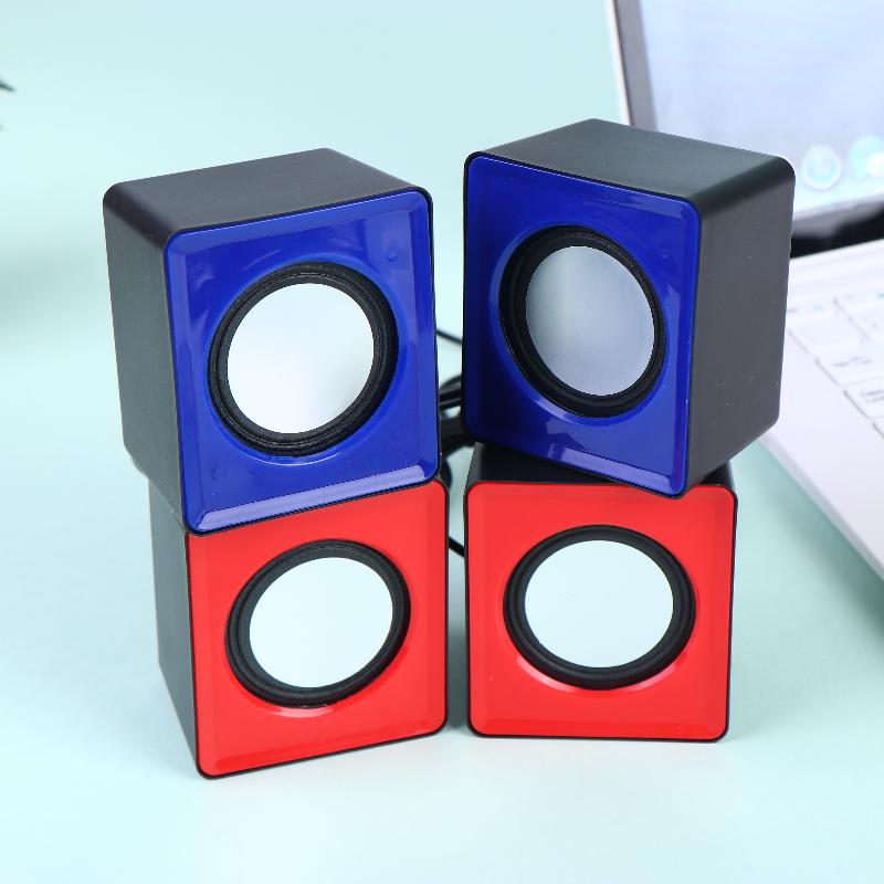 Une paire de mini haut-parleurs de bureau USB présentant un design compact en forme de cube, avec des façades avant bleues et rouges brillantes et des grilles de haut-parleurs noires pour l’audio stéréo sur ordinateur.