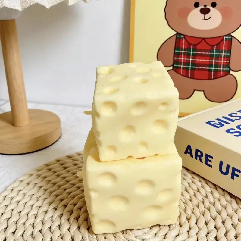 Cream-colored cube-shaped cheese block stress relief squeeze toy with a realistic swiss cheese pattern of holes for stress relief.