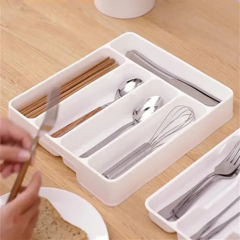Organisateur de tiroir à couverts en plastique blanc, avec des compartiments distincts pour les baguettes, les cuillères, les fourchettes, les couteaux et un fouet, pour le rangement des ustensiles de cuisine.