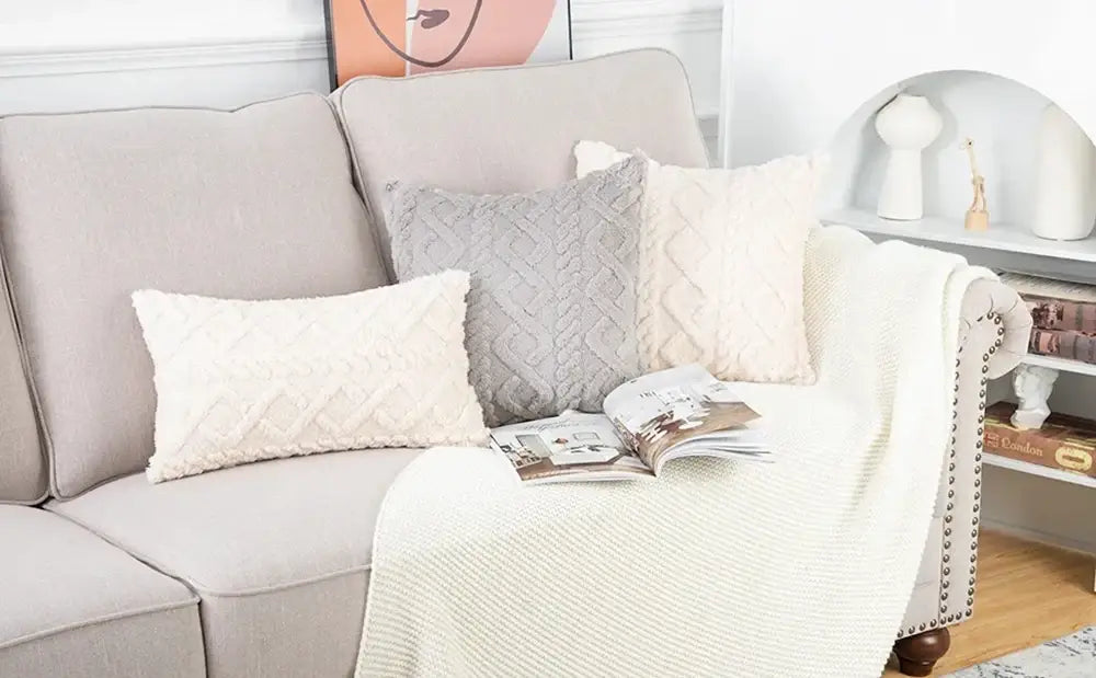 Beige upholstered sofa with cream-colored knit blanket and plush geometric throw pillow cover 45x45cm in textured fabric.