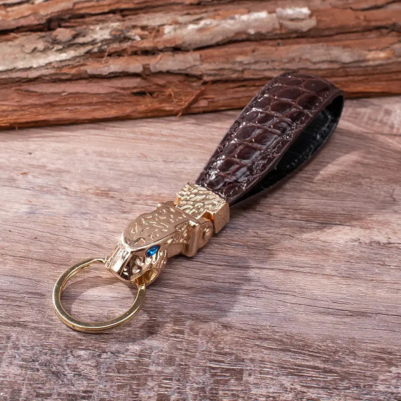 Brown crocodile leather keychain with a gold-toned leopard head charm featuring blue eyes designed as a luxury car key ring.