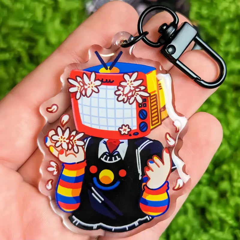 A colorful acrylic tv head anime keychain featuring a cartoon character with a vintage television head, white flowers, and rainbow-striped sleeves, customizable as a bag charm.