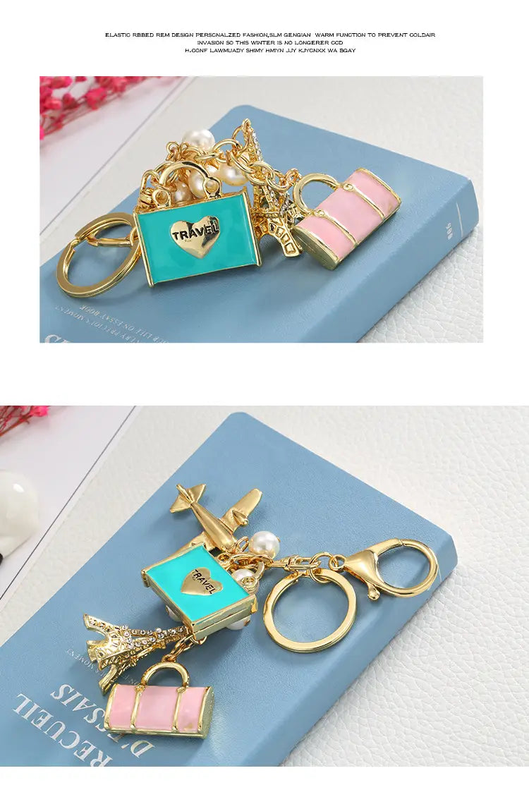 Llavero de viaje en tono dorado con un colgante de corazón de esmalte turquesa, colgantes de bolso rosa y maleta, detalles de perlas y un colgante de avión en miniatura.