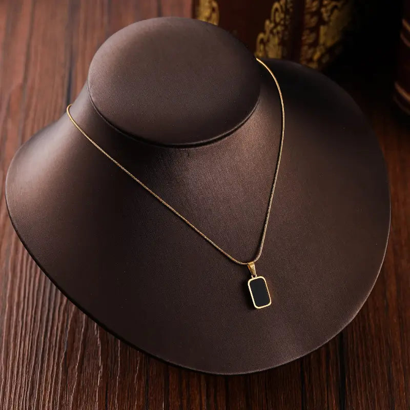 Collier médaillon rectangle en or pour femmes, avec un insert en émail noir présenté sur un présentoir de bijoux brun foncé.