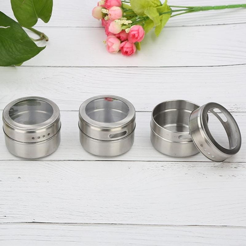 Drei zylindrische Gewürzgläser aus Edelstahl mit klaren Glasdeckeln und gelochten Seiten, angeordnet auf einer weißen Holzoberfläche, aus dem Gewürzgläser-Set aus Edelstahl mit Tablett