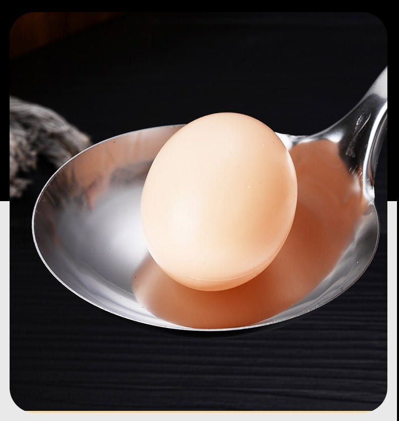 A smooth pale beige egg rests on a shiny stainless steel spoon from a 9-piece kitchen utensil set for cooking.