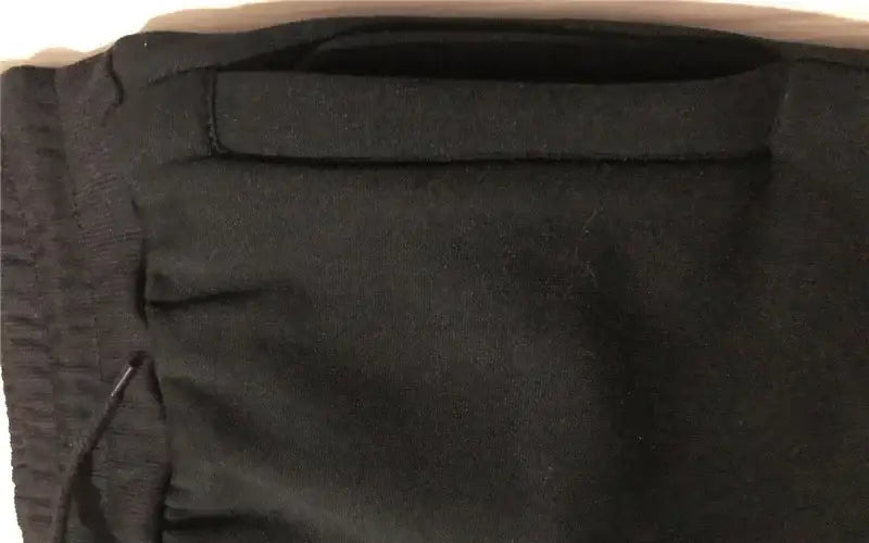 Eine schwarze Stofftasche mit horizontalem Klappenverschluss und sichtbaren Details der Ziernähte, kombiniert mit Herren-Adidas-Sweatpants für sportliches Joggen.