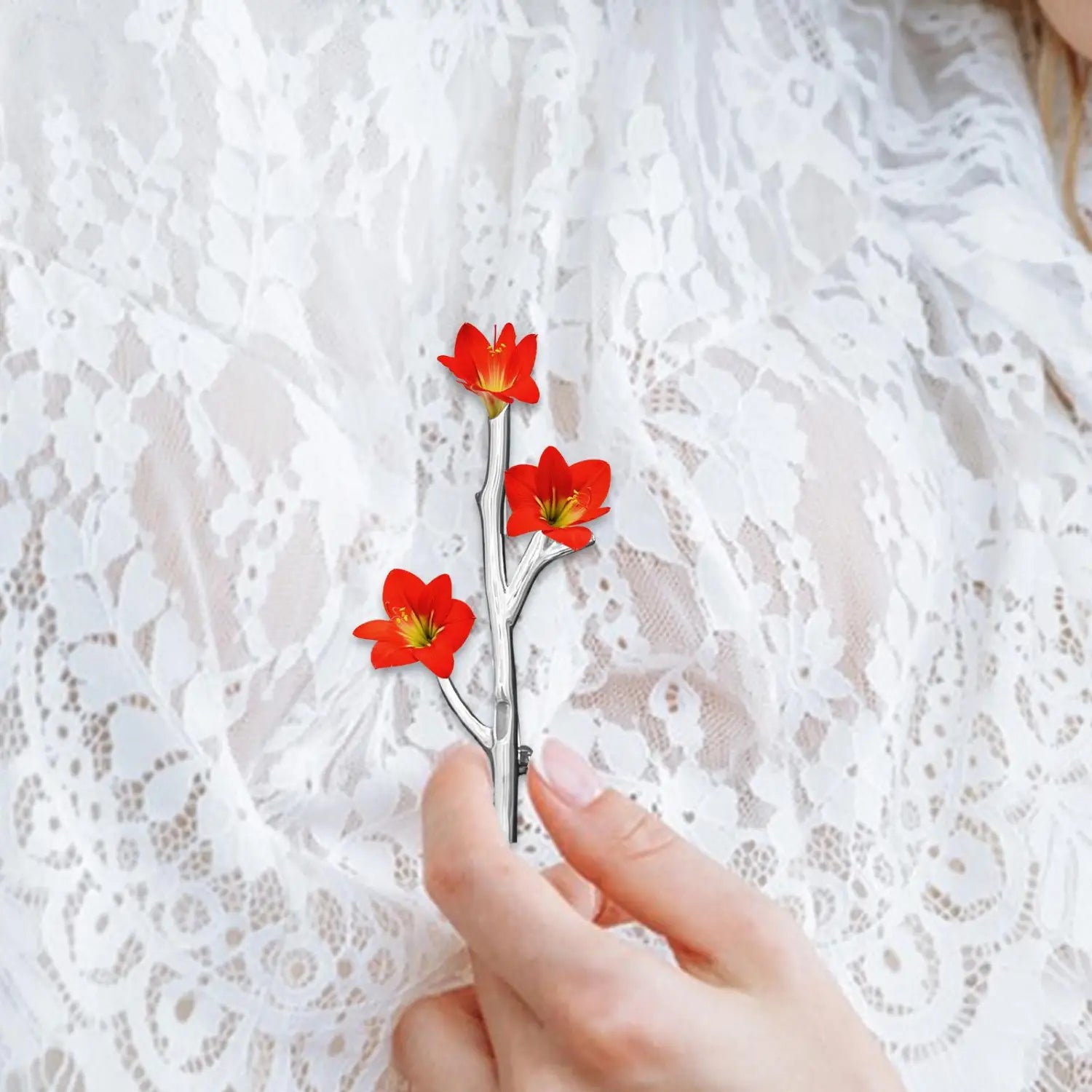 A silver tree branch brooch pin featuring a delicate silver-toned hairpin with three vibrant red flowers with yellow centers designed as a slender branch.