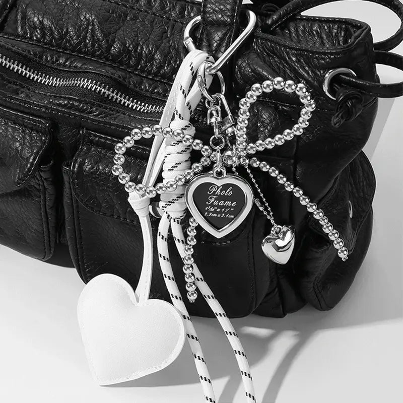Heart pendant bowknot bag keychain featuring a white heart-shaped charm with black and white striped cord and silver beaded accents hanging from a bag strap.