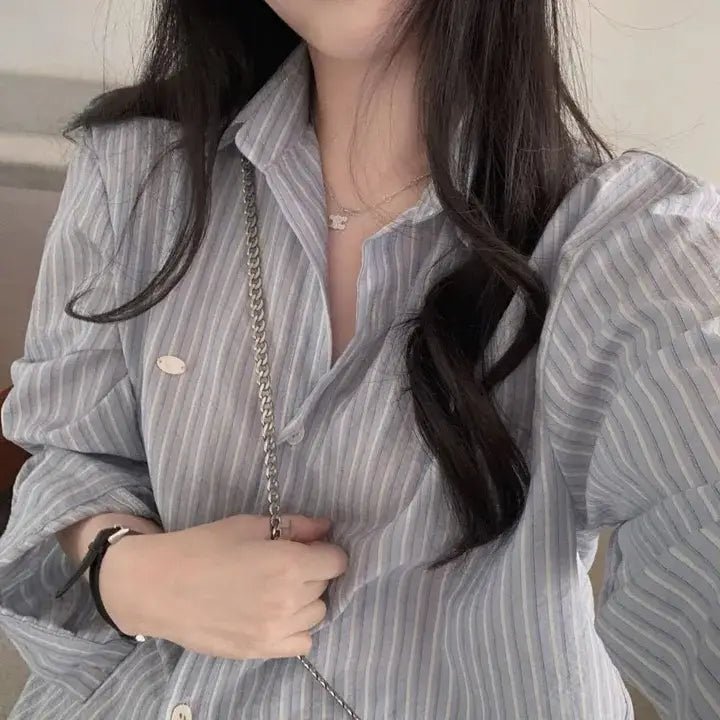 A light gray and white vertically striped long sleeve button down shirt with puffed sleeves featuring a versatile style and standard thickness striped pattern.