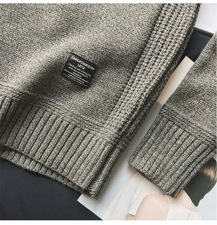 Pull en laine pour homme surdimensionné en maille décontractée, en maille grise texturée, avec poignets côtelés et une étiquette tissée noire comportant du texte blanc.