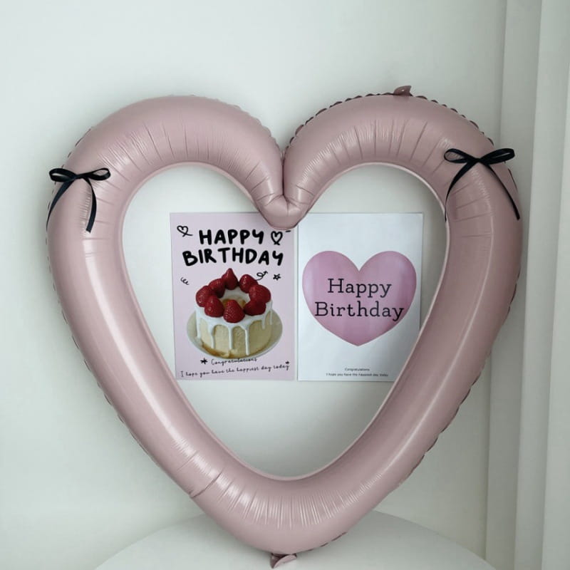 Un globo de lámina para marco de foto de corazón de color rosa suave de 40 pulgadas con lazos de cinta negra que enmarcan dos tarjetas de cumpleaños