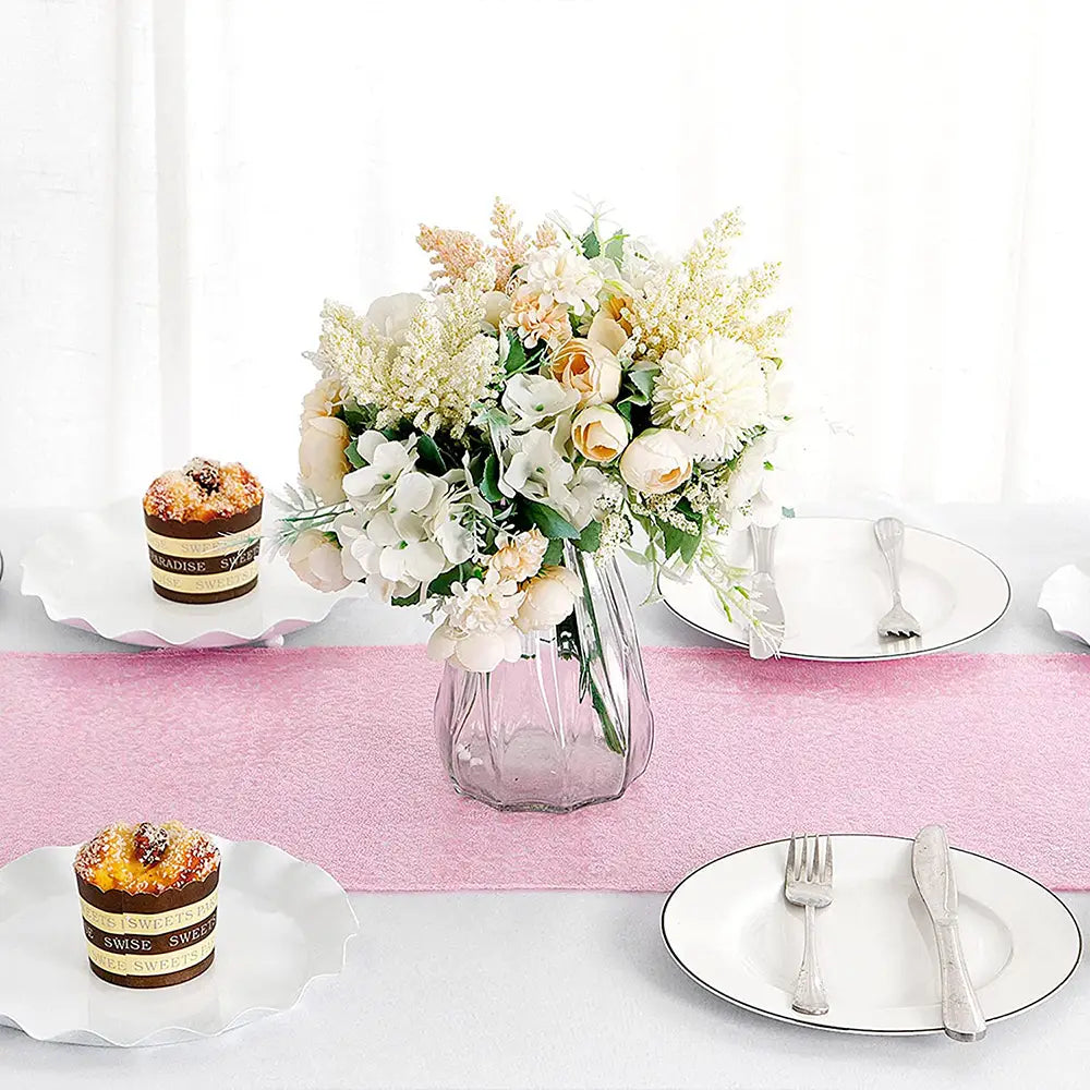A clear faceted glass vase holding a bouquet of white and cream colored artificial flowers displayed with a sequin table runner 12x72 inch party decor.