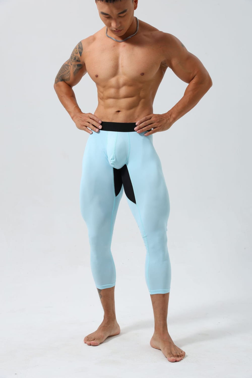 淡いブルーのメンズ用ナイロンフィットネスタイツ、トレーニングパンツ。黒いウエストバンドと中央のファブリックパネルを備え、体にフィットする3／4丈のデザインが特徴です