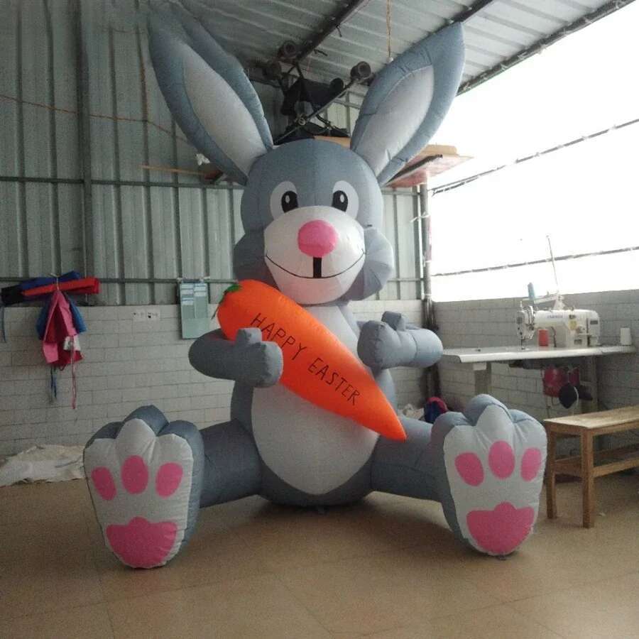 A gray inflatable Easter bunny party decoration with a pink nose and paw pads holding an orange carrot reading happy Easter.