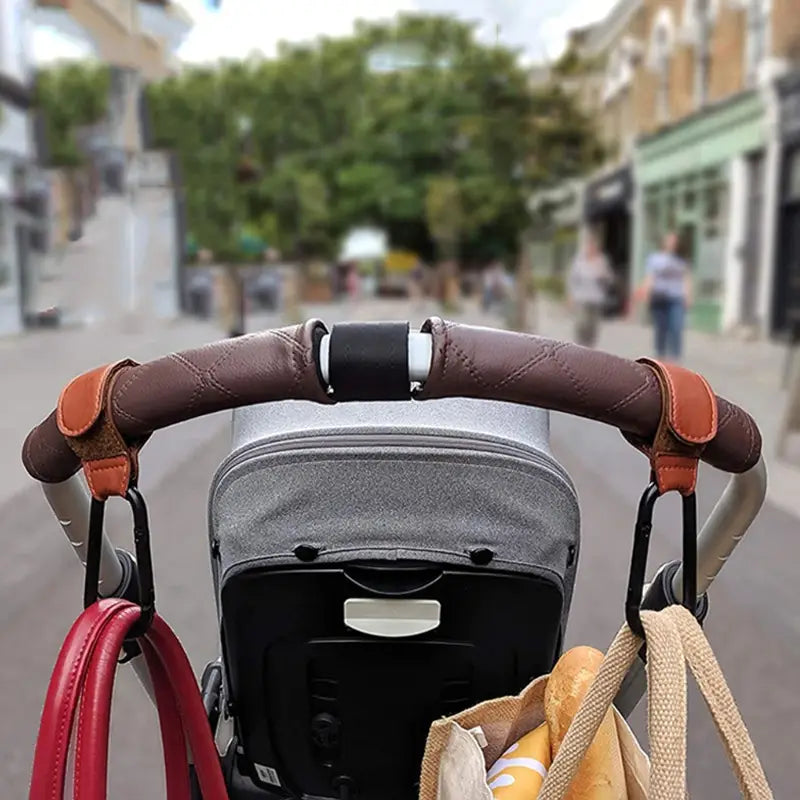 braune wattierte PU-Ledernhaken für den Kinderwagen mit beigen Akzenten und schwarzen Metallhaken für eine verstellbare Aufhängung der Kinderwagen-/Buggytasche